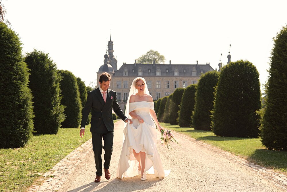 Bride and groom walking along the yew alley in front of Chateau de Mirwart
