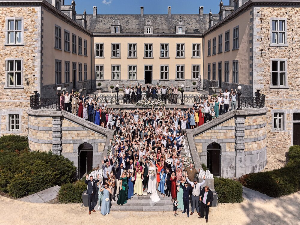 The main facade and twin staircases of Chateau de Mirwart from the air, the whole wedding party on the steps
