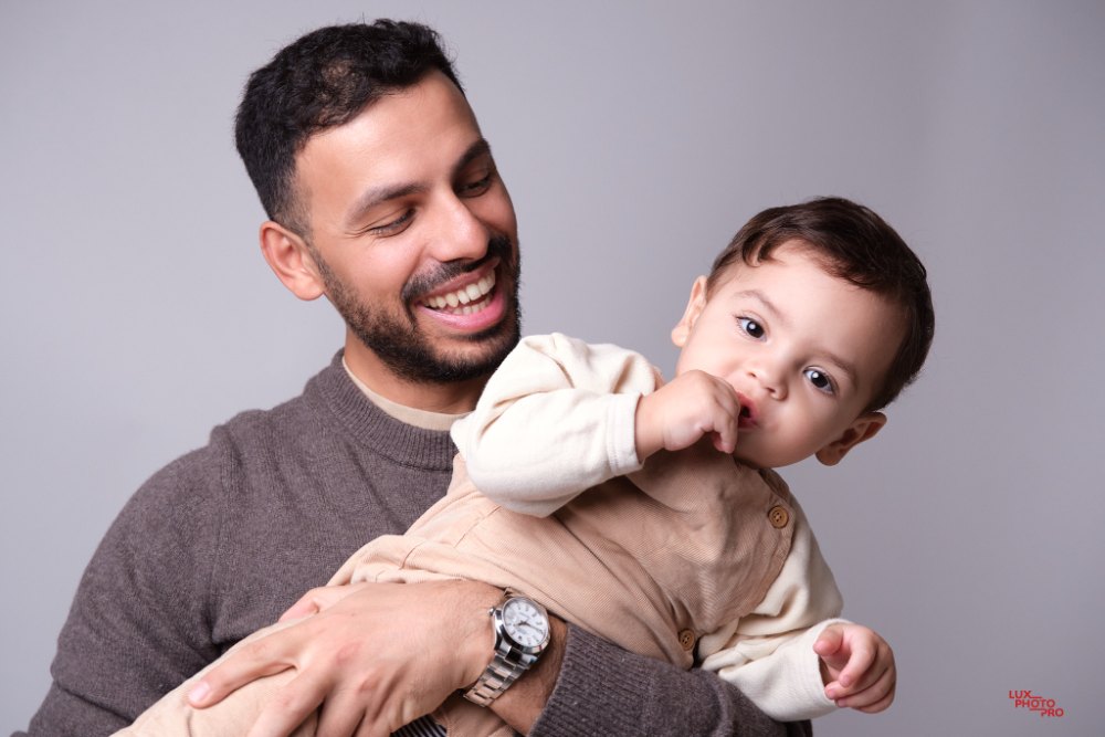 A father holding his smiling toddler against a grey studio backdrop